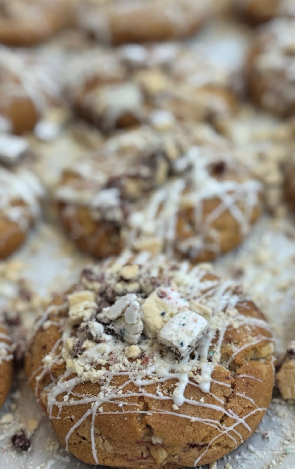 Close-up of cookies with white drizzle and crumbly topping on a baking sheet.